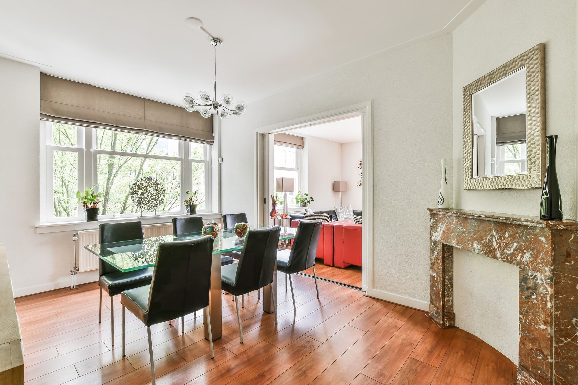 Dining room with a glass table, black chairs, a marble fireplace and timber floors