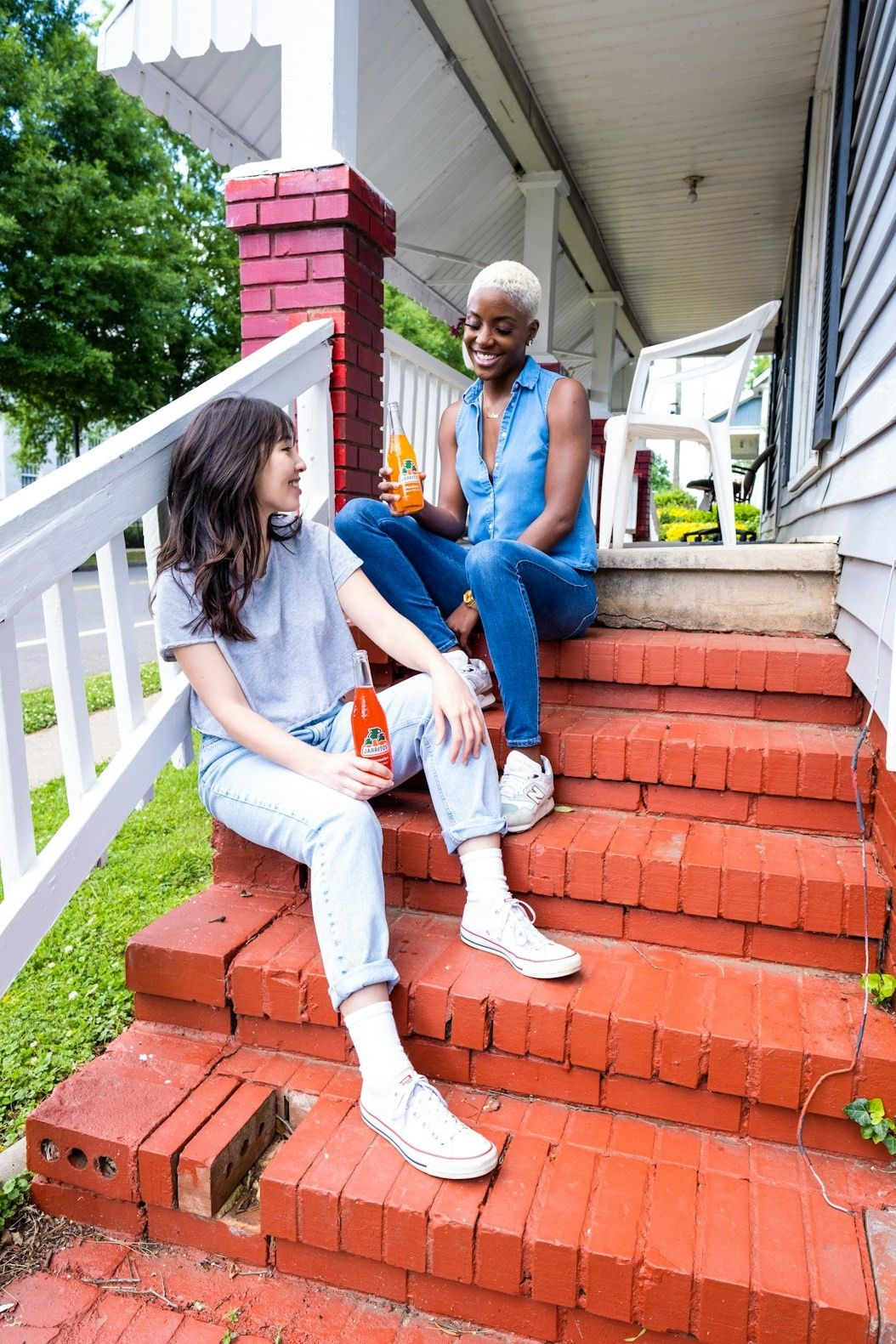 Two friends sitting on red brick steps of a white timber house porch