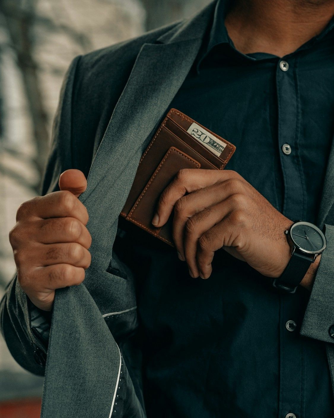 A man in a dark jacket taking a leather wallet from his inside pocket