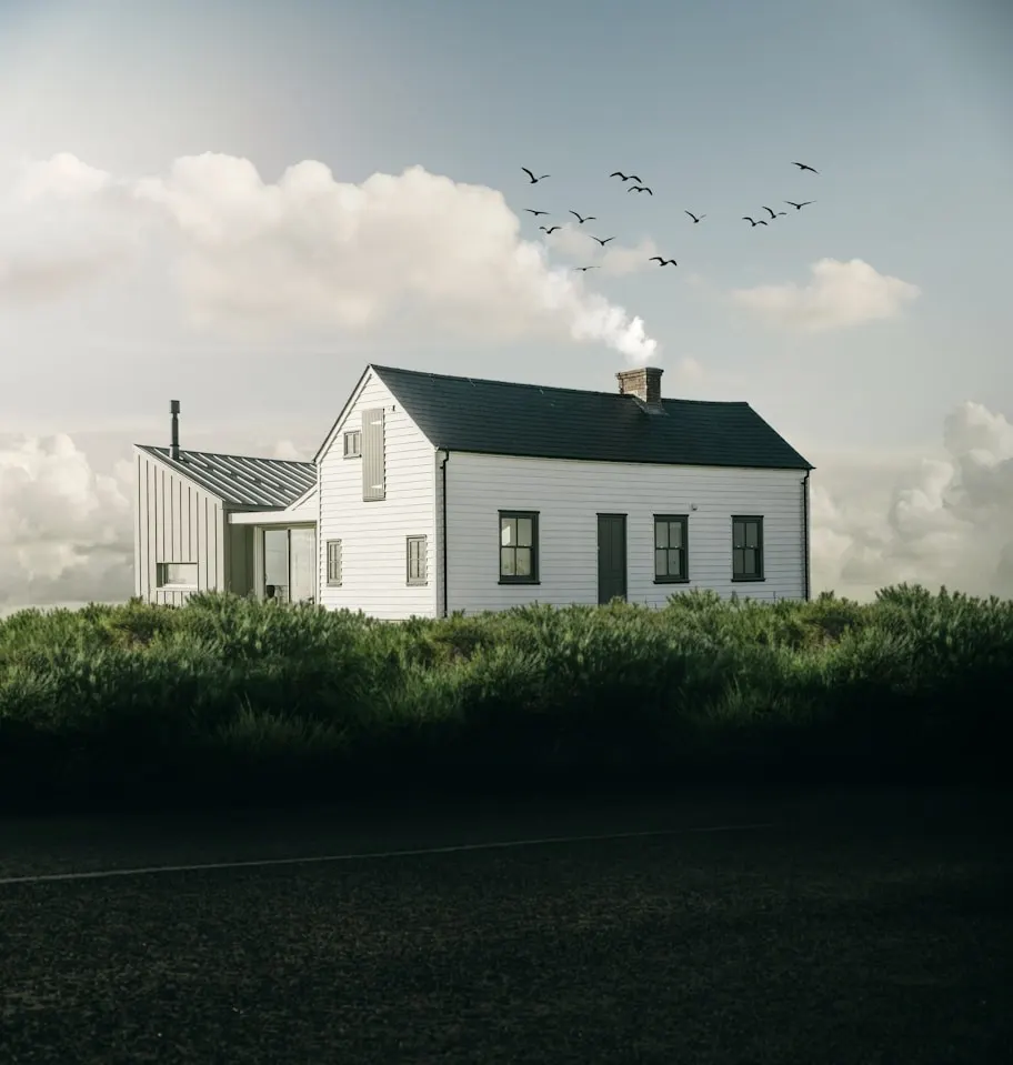White weatherboard farmhouse with a dark roof and attached studio, behind tall grasses